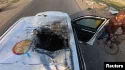 A Palestinian man rides a bicycle past a damaged vehicle where employees from the World Central Kitchen were killed in an Israeli airstrike, according to the NGO, in Deir al-Balah, Gaza Strip, April 2, 2024. 