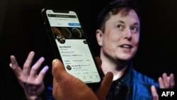 FILE - In this photo illustration, a phone screen displays the Twitter account of Elon Musk with a photo of him shown in the background, in Washington, D.C., April 14, 2022.