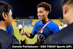 Jwe seleksyon Ameriken Tyler Adams siyen balon foutbol pou travaye migran yo pandan yon evenman kominote nan stad Al Gharrafa a, nan Doha, Qatar.