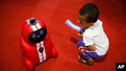 Một em bé cầm vé vào cửa ngồi nhìn môt robot tự học tinh khôn tại Hội nghị Robot Thế giới 2017 ở Bắc Kinh, ngày 23/8/2017. 