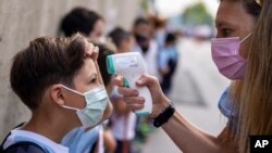 FILE - A teacher wearing a face mask to protect against the spread of coronavirus checks the temperature of her student at Maestro Padilla school as the new school year begins, in Madrid, Sept. 7, 2021. With one of Europe's highest vaccination rates and i