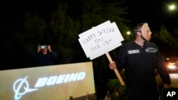 A Boeing worker wears a mask while holding a 'Happy Strike Day' sign after union members voted overwhelmingly to reject a contract offer and go on strike Sept. 13, 2024, outside the company's factory in Renton, Wash. 